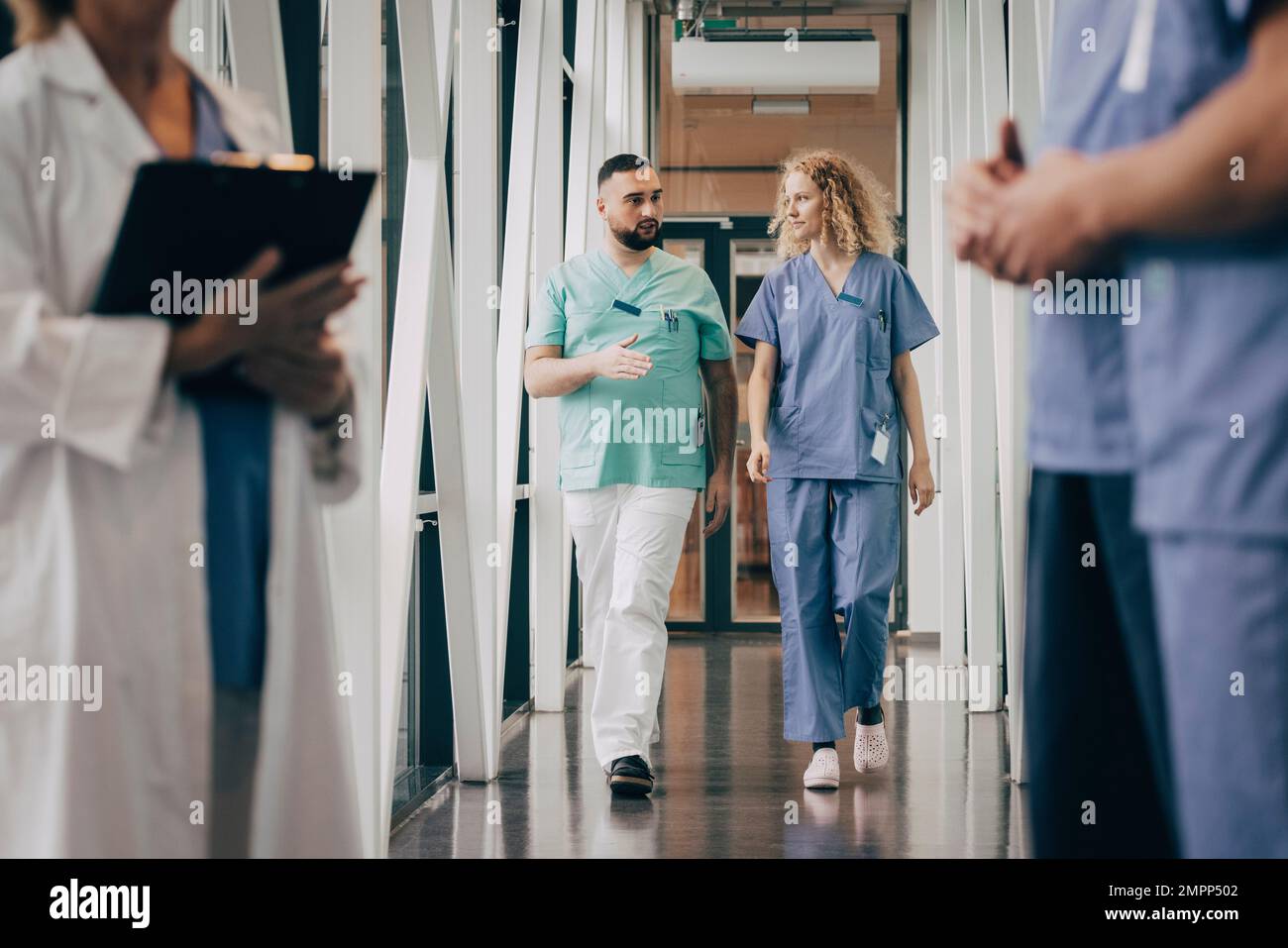 Männlicher Arzt erklärt Kollege beim Gehen im Flur des Krankenhauses Stockfoto