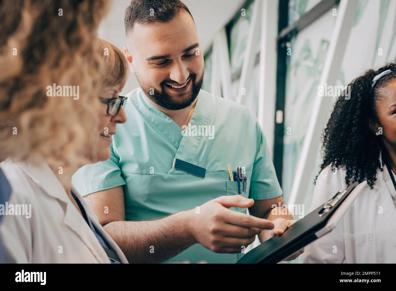Lächelnder männlicher Gesundheitshelfer diskutiert mit Arzt über Klemmbrett im Krankenhaus Stockfoto