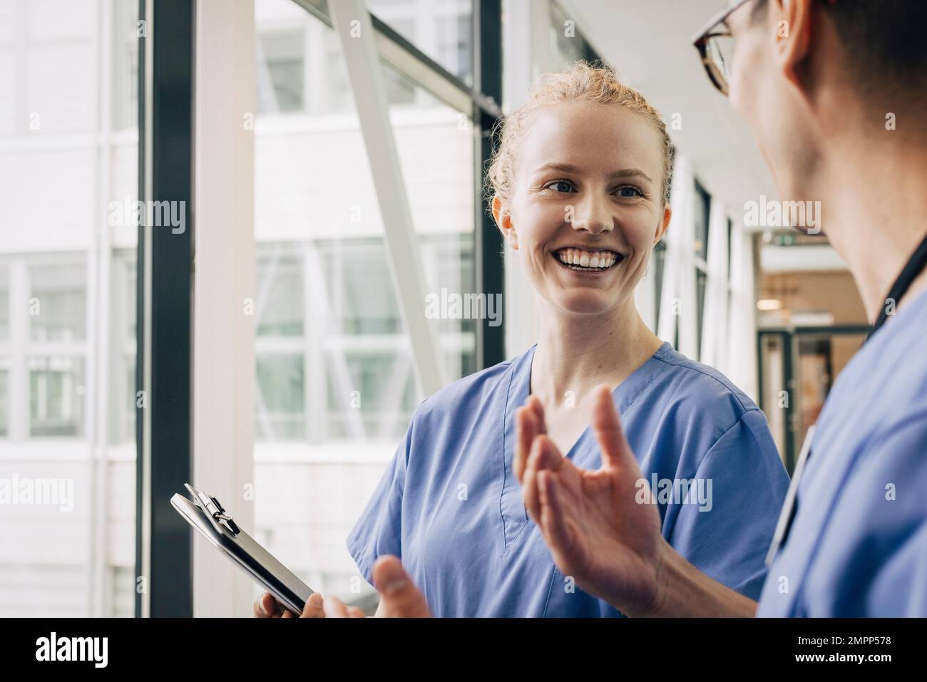 Glückliche junge Krankenschwester, die mit männlichem Kollegen im Krankenhaus spricht Stockfoto