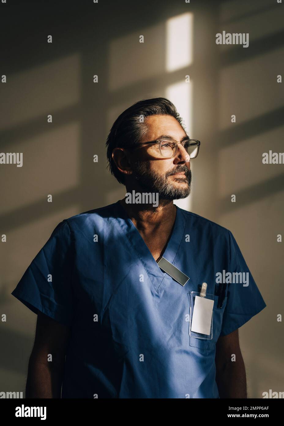 Reifer männlicher Arzt, der wegschaut, während er im Krankenhaus an der Wand steht Stockfoto