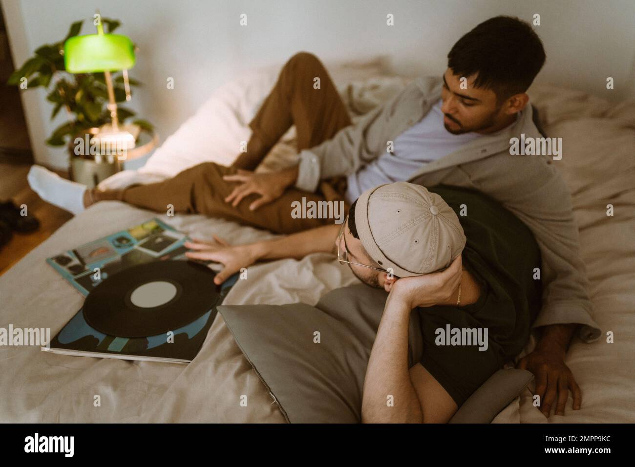 Schwules Paar mit Schallplatte, das sich zu Hause im Bett unterhält Stockfoto