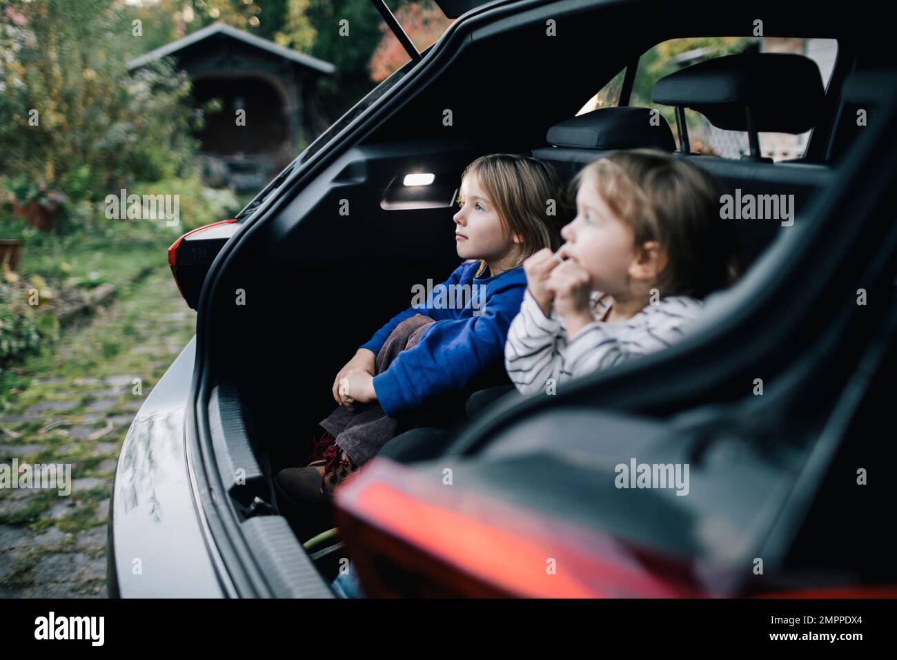 Mädchen träumt von Schwester, während sie im Kofferraum eines Elektroautos sitzt Stockfoto