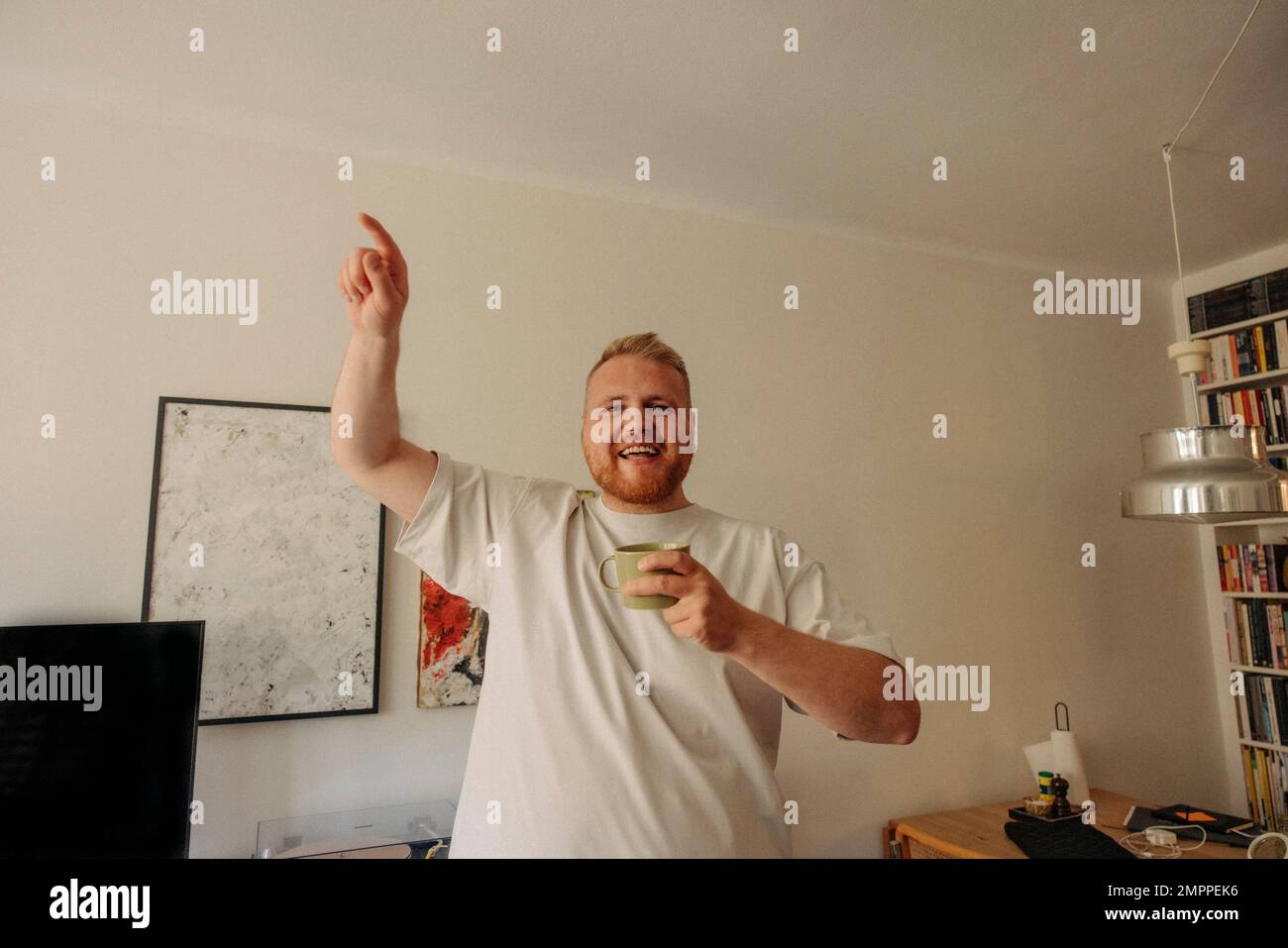 Porträt eines glücklichen, übergewichtigen Mannes, der zu Hause tanzt und einen Becher hält Stockfoto