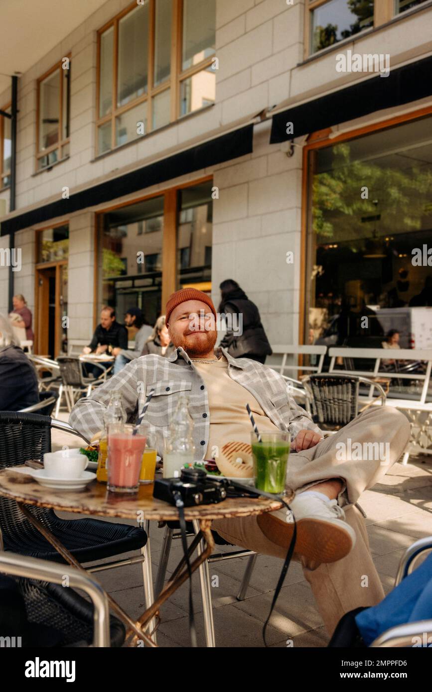 Lächelnder fettleibiger Mann, der mit Drinks auf dem Tisch im Straßencafé saß Stockfoto