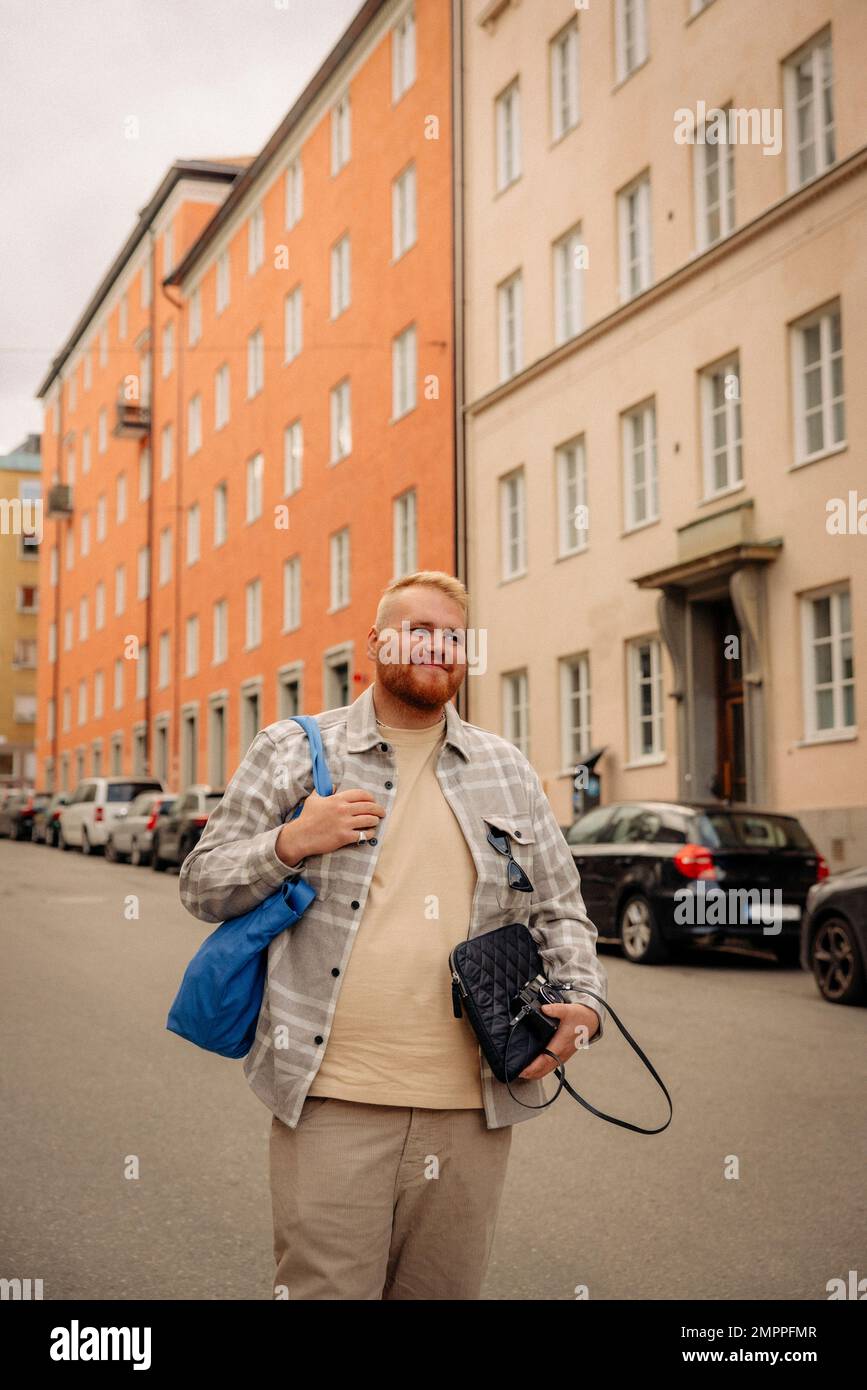 Lächelnder fettleibiger Mann mit Tasche, der vor dem Gebäude auf der Straße läuft Stockfoto