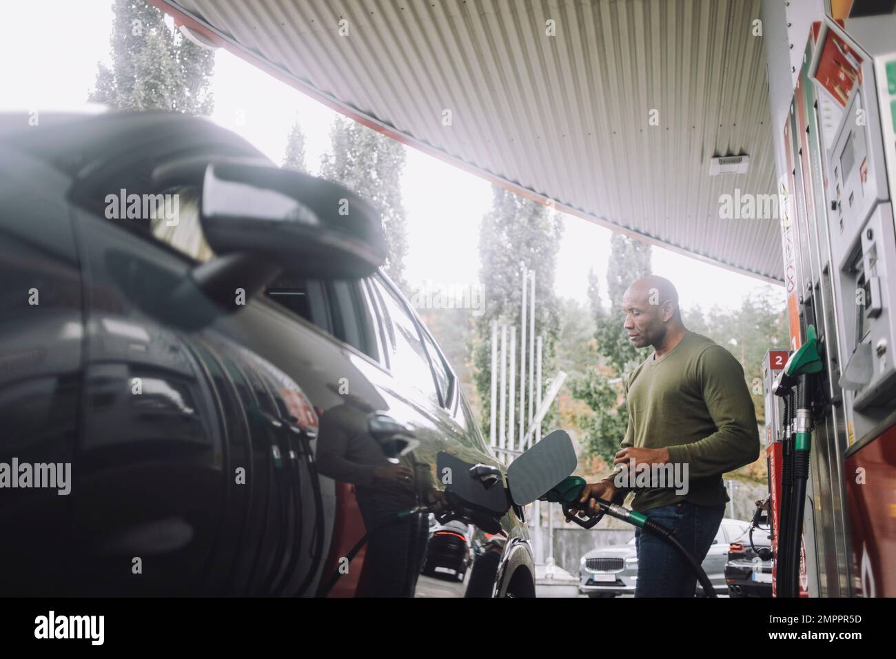 Ein erwachsener Mann betankt ein Fahrzeug, während er an der Tankstelle steht Stockfoto