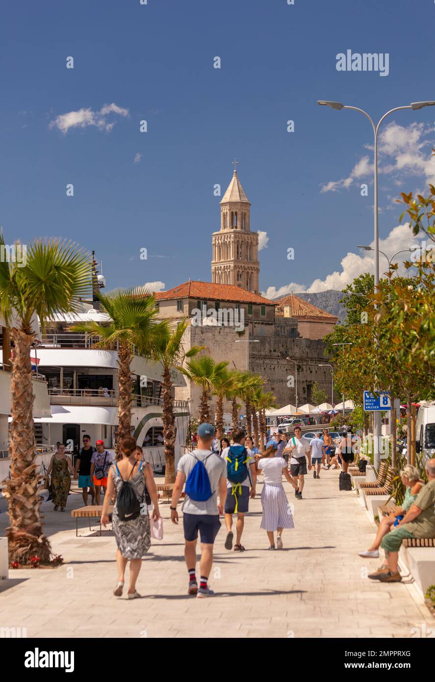SPLIT, KROATIEN, EUROPA - Touristen laufen am Ufer entlang. In der Ferne befindet sich der Glockenturm der Kathedrale des Heiligen Domnius. Stockfoto