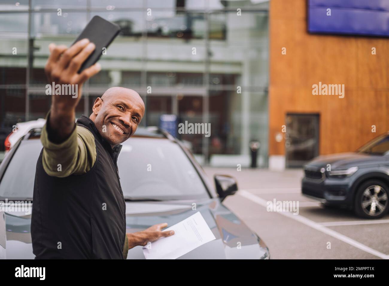 Glücklicher Mann, der nach dem Kauf eines neuen Autos Selfie über das Smartphone macht Stockfoto