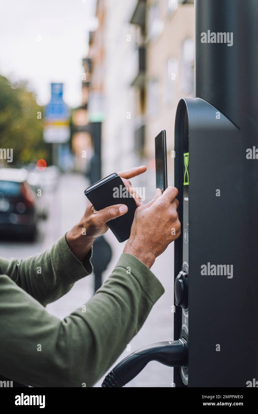 Hände eines Mannes, der mobile Zahlungen an der Ladestation tätigt Stockfoto
