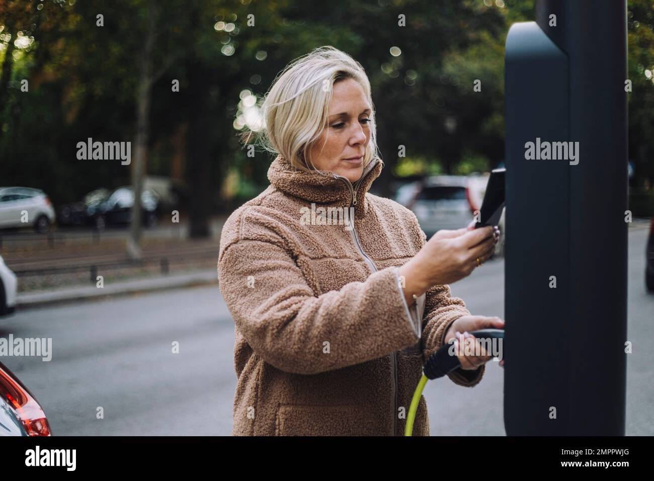 Frau, die das Ladegerät hält, während sie das Smartphone an der Ladestation durchsucht Stockfoto