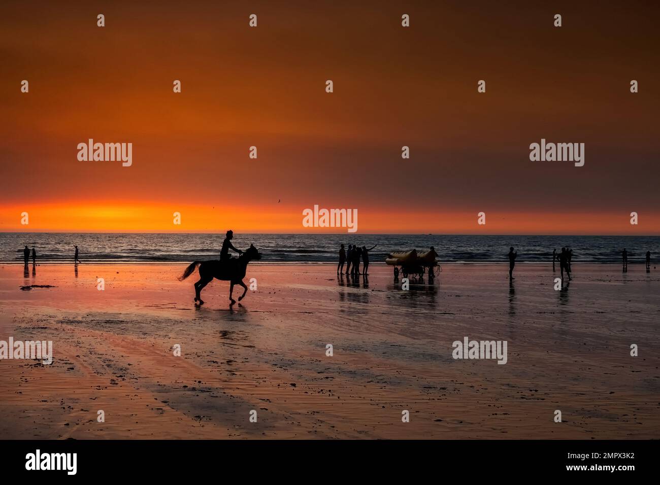 Silhouette von Reitern und Silhouette von Menschen, die den Sonnenuntergang am Murud Beach in der Nähe von Dapoli Maharashtra genießen. Farbenfroher orangefarbener, warmer Himmel nach dem Sonnenuntergang. Stockfoto