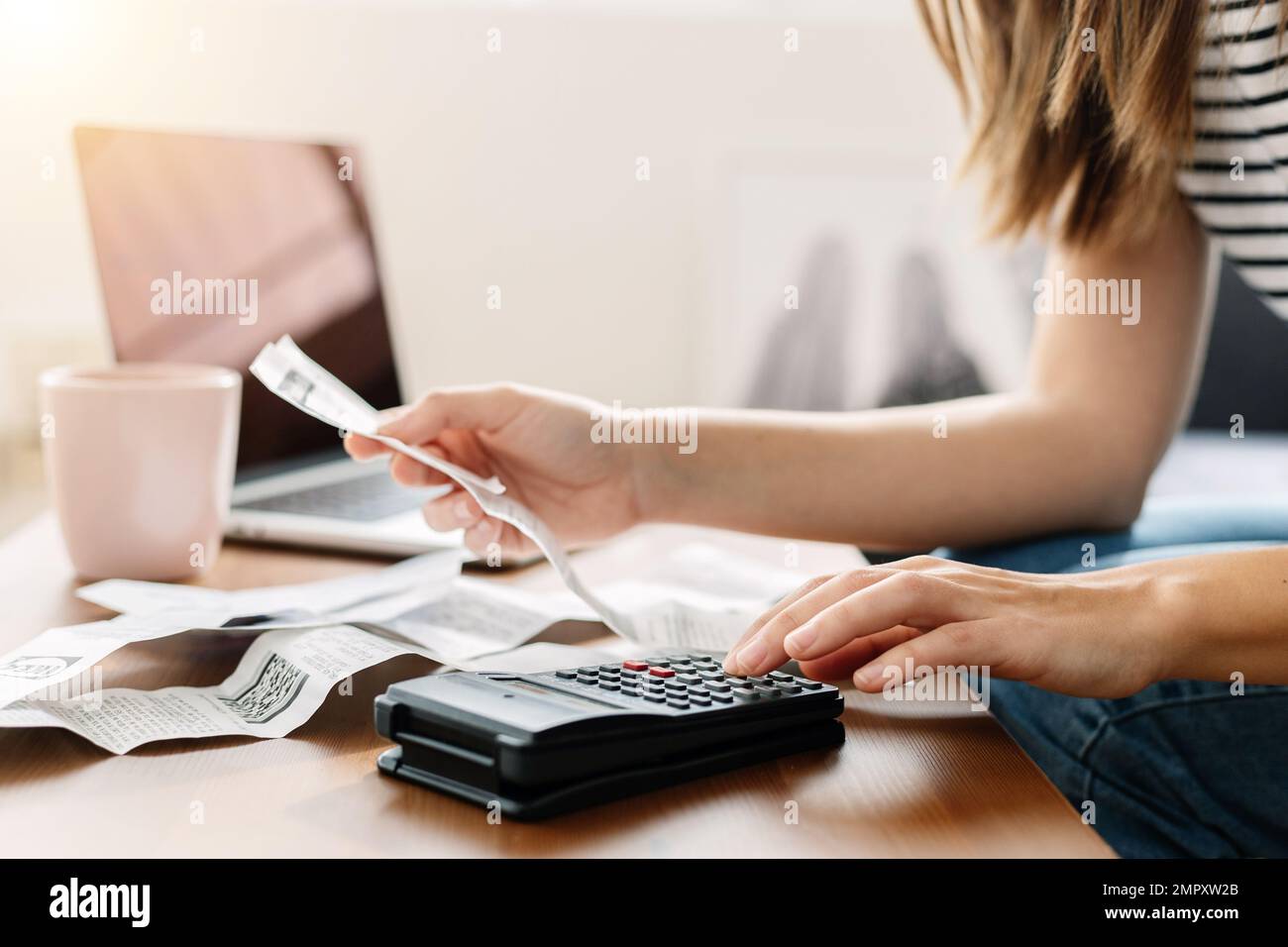 Junge Frau, die auf dem Sofa sitzt und den Taschenrechner zur Berechnung der Haushaltsausgaben verwendet Stockfoto