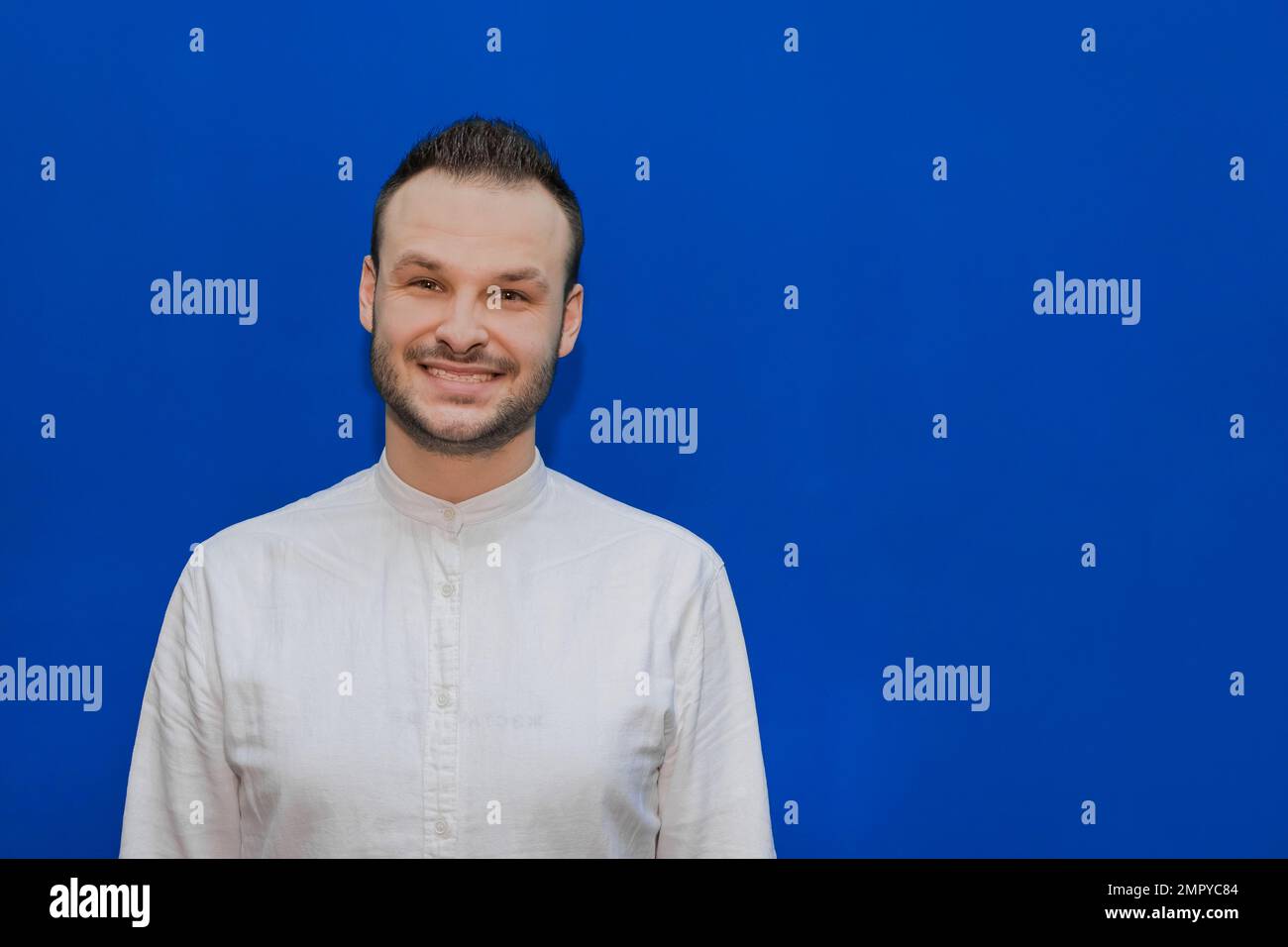 Ein positiver und fröhlicher Kerl, kaukasisches Aussehen, stilvoller Geschäftsmann in einem weißen Hemd auf blauem Hintergrund. Stockfoto