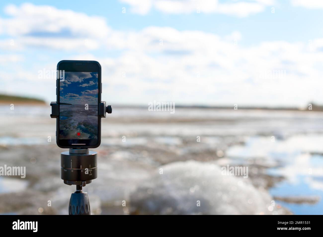 Ein Mobiltelefon macht ein Foto des Frühlingseises während des Tages auf einem Stativ mit Schwenkmechanismus für Panoramaaufnahmen. Stockfoto