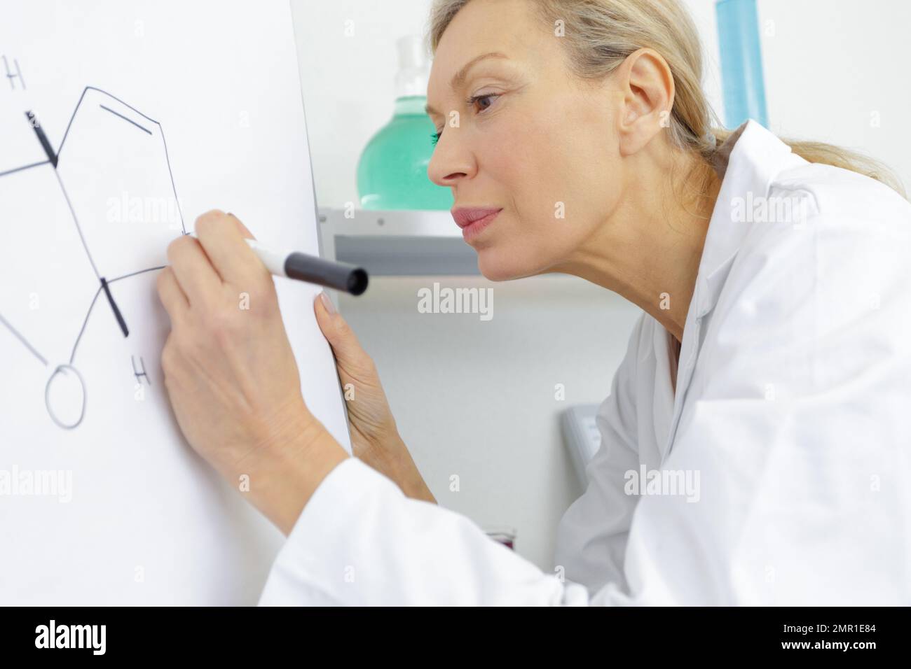 Lehrerin, die im Klassenzimmer Mathematikformeln an der Tafel schreibt Stockfoto