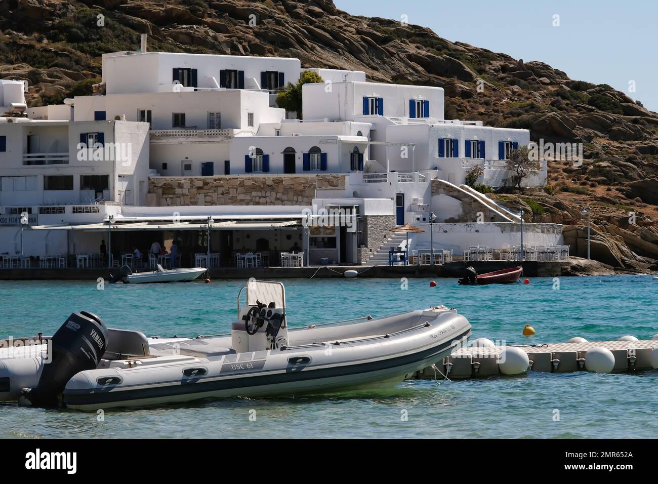 IOS, Griechenland - 3 . Juni 2021 : Blick auf ein Schnellboot, ein weiß getünchtes Hotel und eine Meeresfrüchtetraverne vor dem berühmten Mylopotas-Strand in iOS Greece Stockfoto