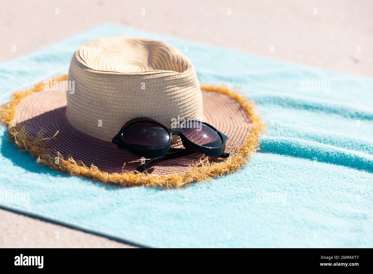 Nahaufnahme von Sonnenbrille und Hut auf blauem Handtuch am Strand an sonnigen Tagen Stockfoto
