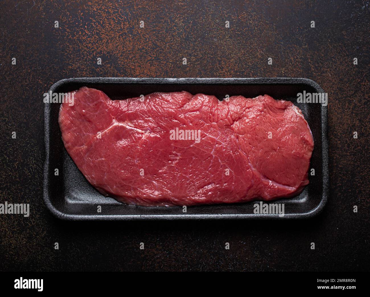 Rind mageres Filet Steak in schwarzem Kunststoffbehälter auf dunkelbraunem rustikalem Betonhintergrund von oben flach liegend, Diät Rindfleisch Steak fertig für C Stockfoto