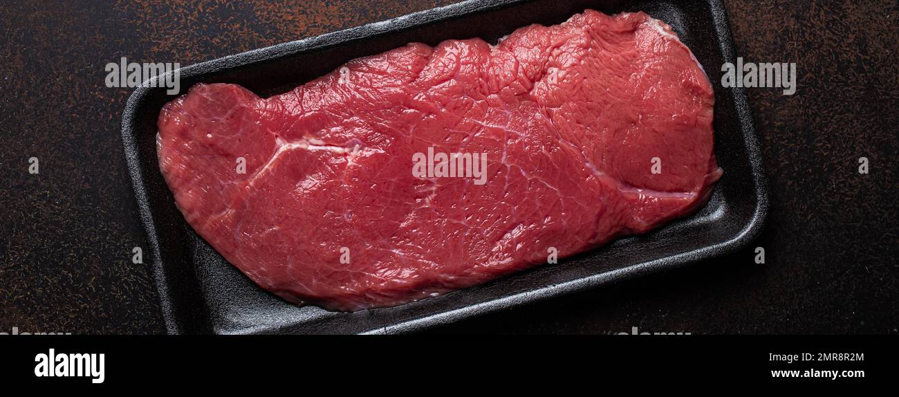 Rind mageres Filet Steak in schwarzem Kunststoffbehälter auf dunkelbraunem rustikalem Betonhintergrund von oben flach liegend, Diät Rindfleisch Steak fertig für C Stockfoto