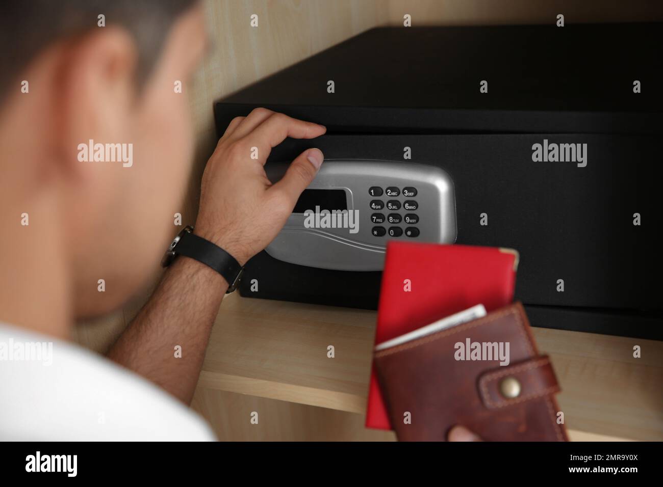 Mann öffnet schwarzen Stahlsafe mit elektronischem Schloss im Hotel, Schließung Stockfoto