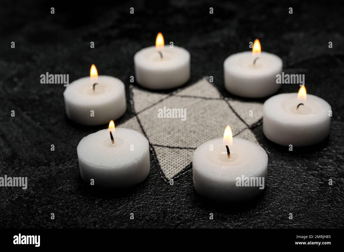 Brennende Kerzen und jüdische Marke auf dunklem Hintergrund. Internationaler Holocaust-Gedenktag Stockfoto