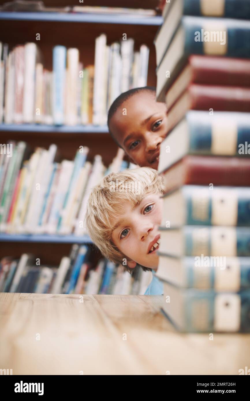 Hallo. Zwei Schulkinder, die in der Bibliothek um einen Stapel Bücher gucken. Stockfoto