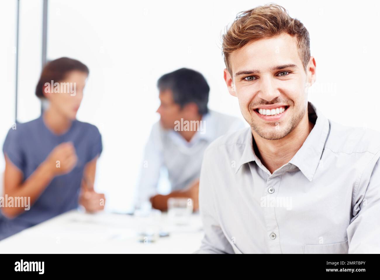 Ich bin stolz, ein Mitglied dieses Teams zu sein. Nahaufnahme eines lächelnden jungen Geschäftsmannes mit seinen Kollegen im Hintergrund. Stockfoto
