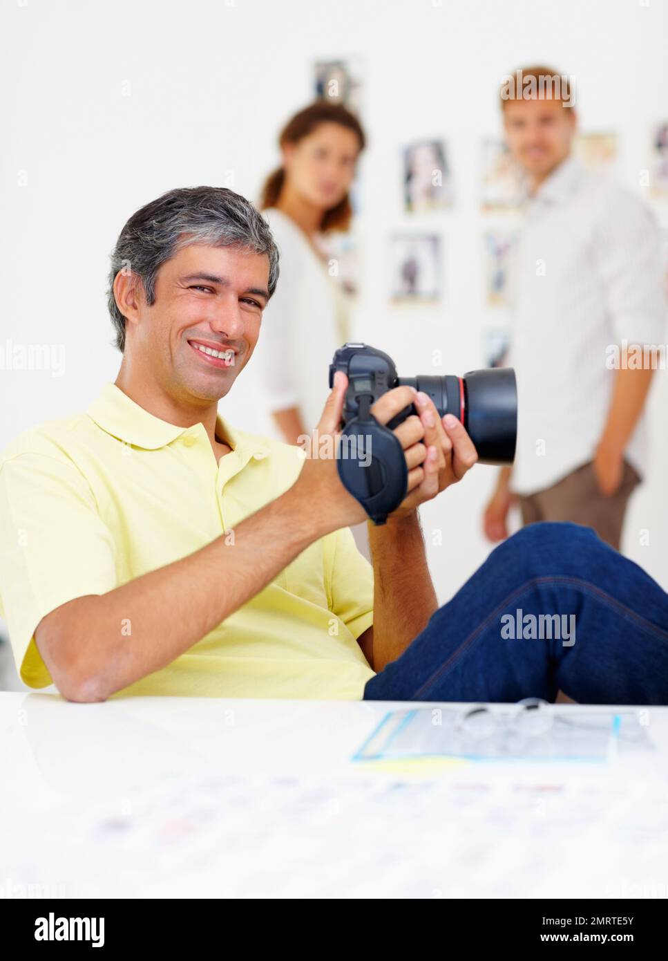 Ein gutaussehender Mann, der sich Bilder in der Kamera ansieht. Porträt eines gutaussehenden Mannes, der Bilder in der Kamera betrachtet und mit Menschen im Hintergrund lächelt. Stockfoto