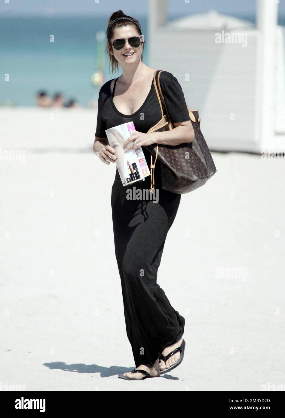 Der argentinische Schauspieler Fabian Mazzei umarmt seine Freundin, das argentinische Modell und die Schauspielerin Araceli Gonzalez, während sie eine schöne Zeit mit der Familie am Strand von Miami verbringen. Gonzalez, die für Fotografen lächelte, als sie in ihrem langen schwarzen Cover vom Strand wegging, schien sehr glücklich zu sein, als sie ihre Louis Vuitton Tragetasche und das Nylon Magazin trug. Miami, Florida 10/02/10. Stockfoto