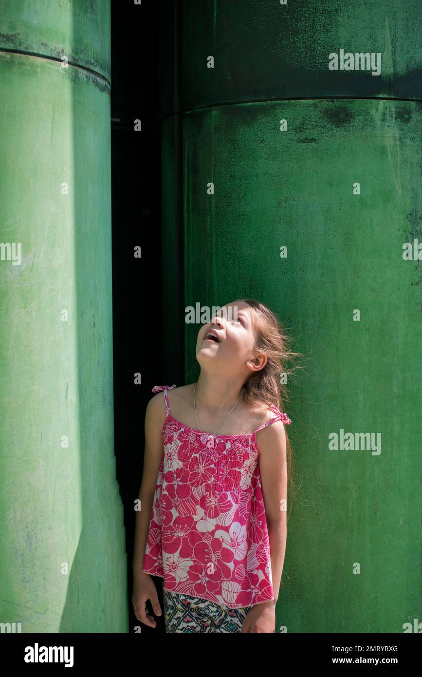 Ein kleines Mädchen wundert sich, zwischen zwei riesigen grünen Säulen hinaufzuschauen Stockfoto