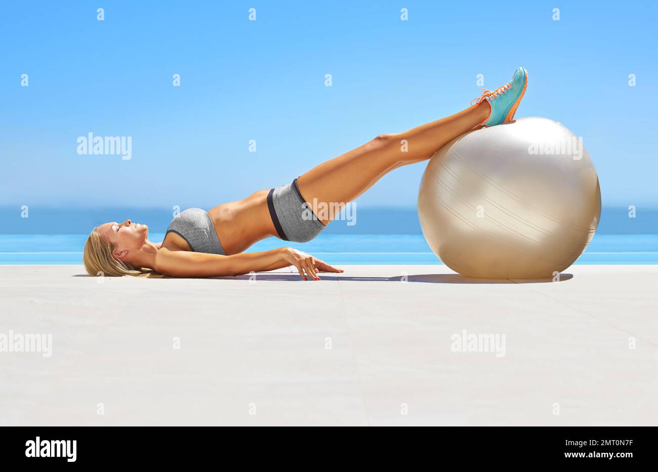 Fitness für den ganzen Körper. Eine attraktive junge Frau, die mit einem Sportball am Pool trainiert. Stockfoto