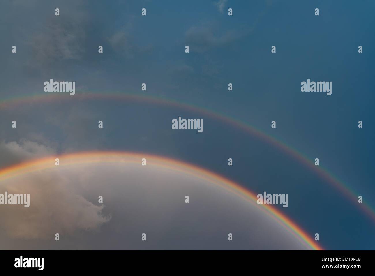 Doppelter Regenbogen vor einem dunkelblauen Himmel und weiße Wolken nach Regen während des Tages. Stockfoto