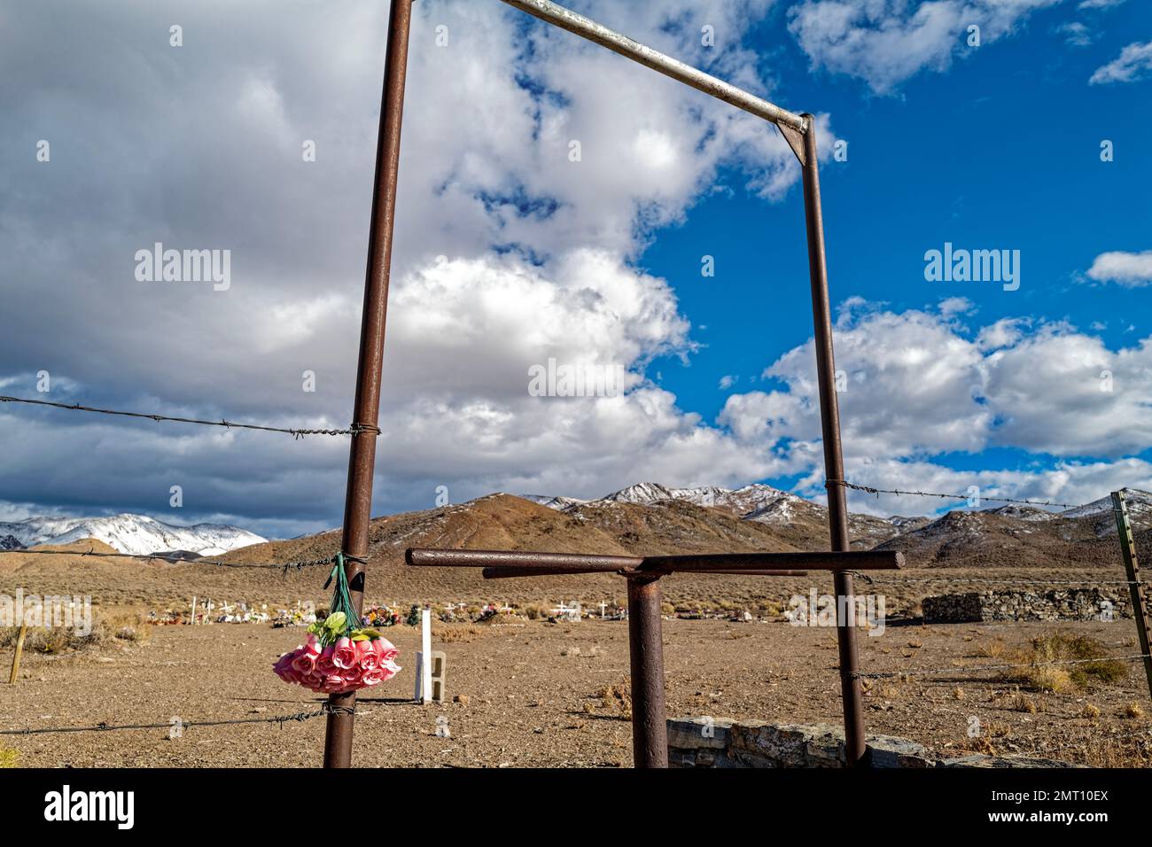 Neben dem rostigen Drehkreuz eines Wüstenfriedhofs im Westen Nevadas, USA, hängen künstliche Blumen Stockfoto