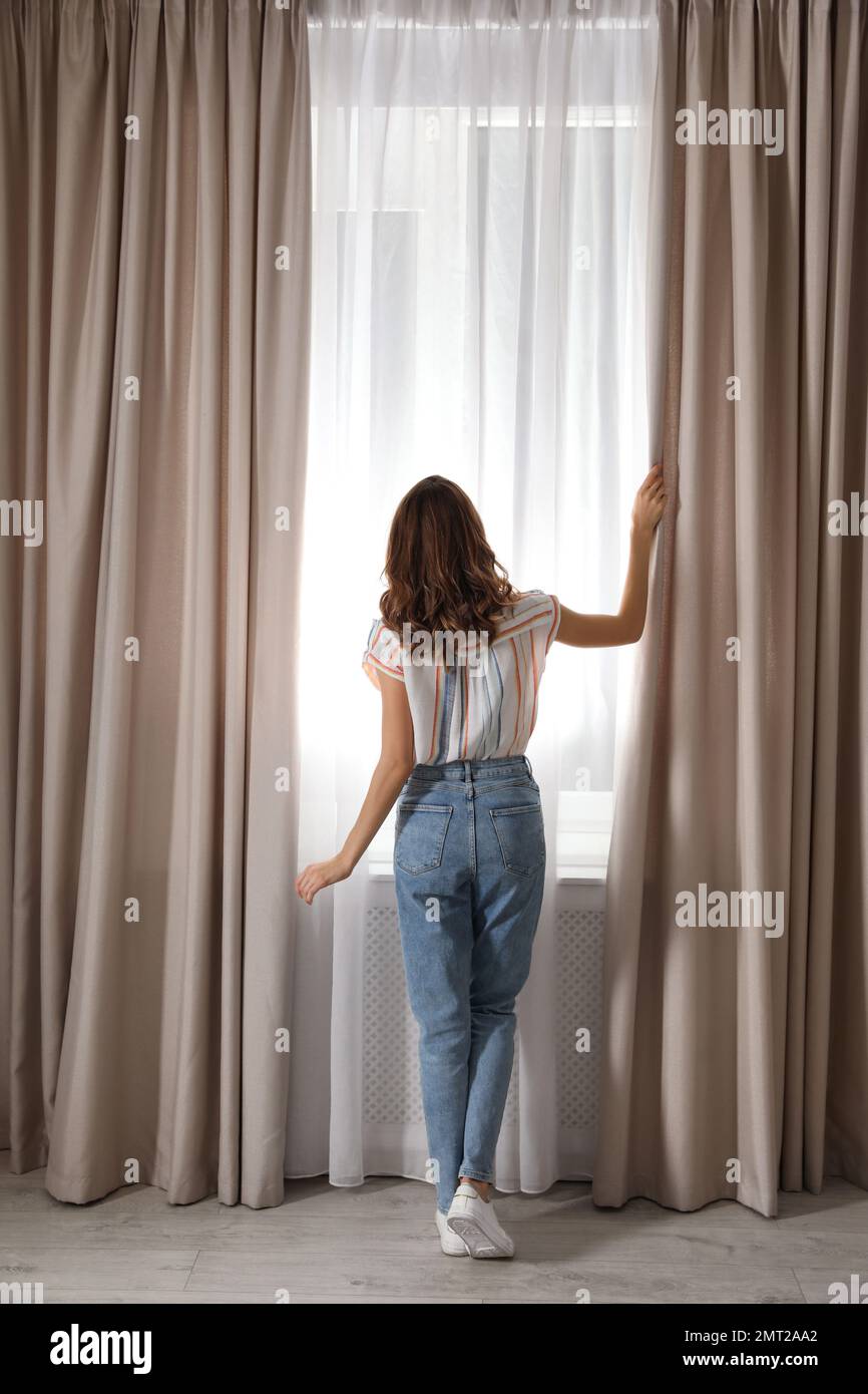 Frau öffnet morgens zu Hause die Vorhänge, Rückansicht Stockfoto