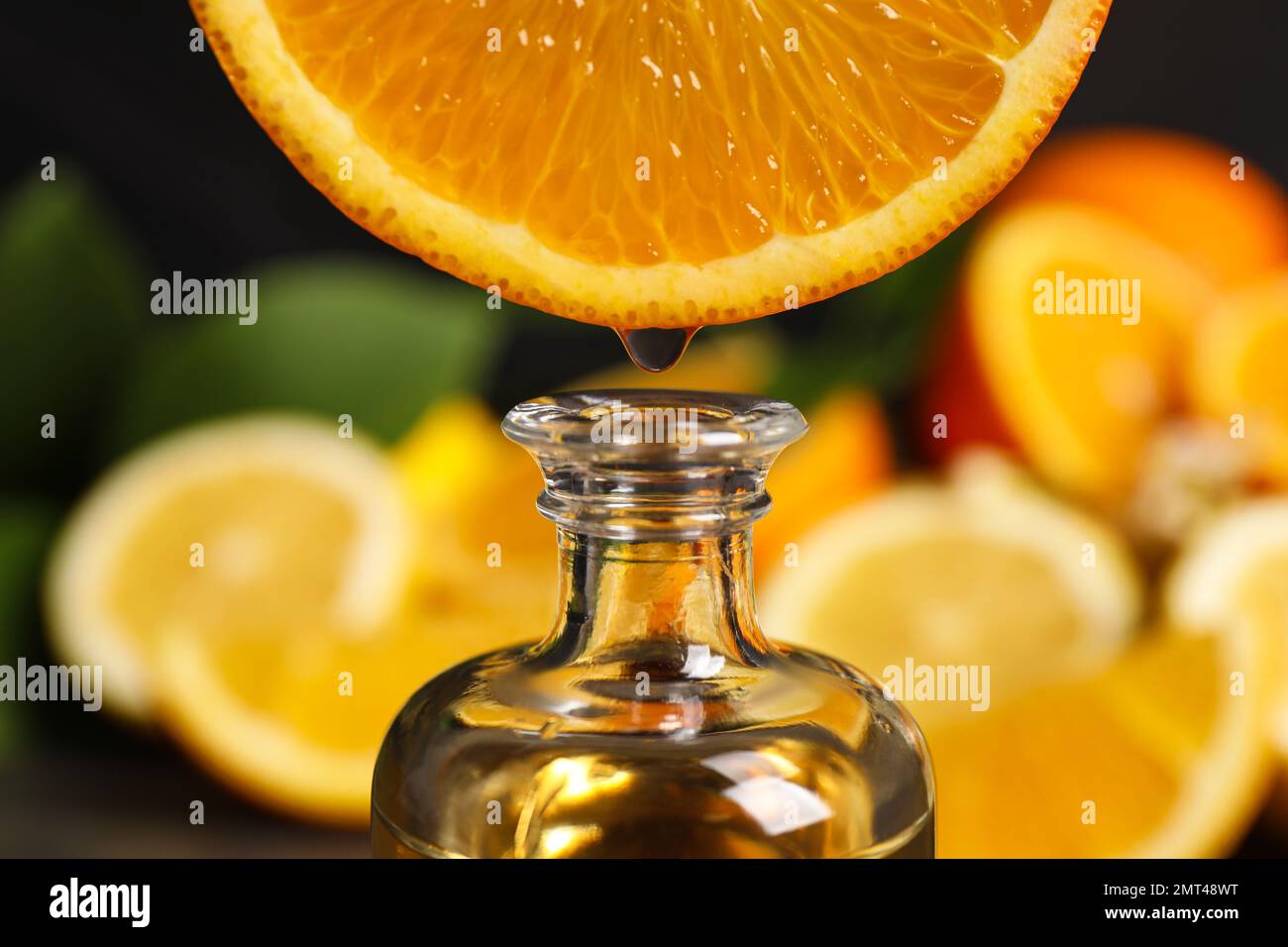 Ätherisches Zitrusöl tropft aus der Orangenscheibe in die Flasche, Nahaufnahme Stockfoto