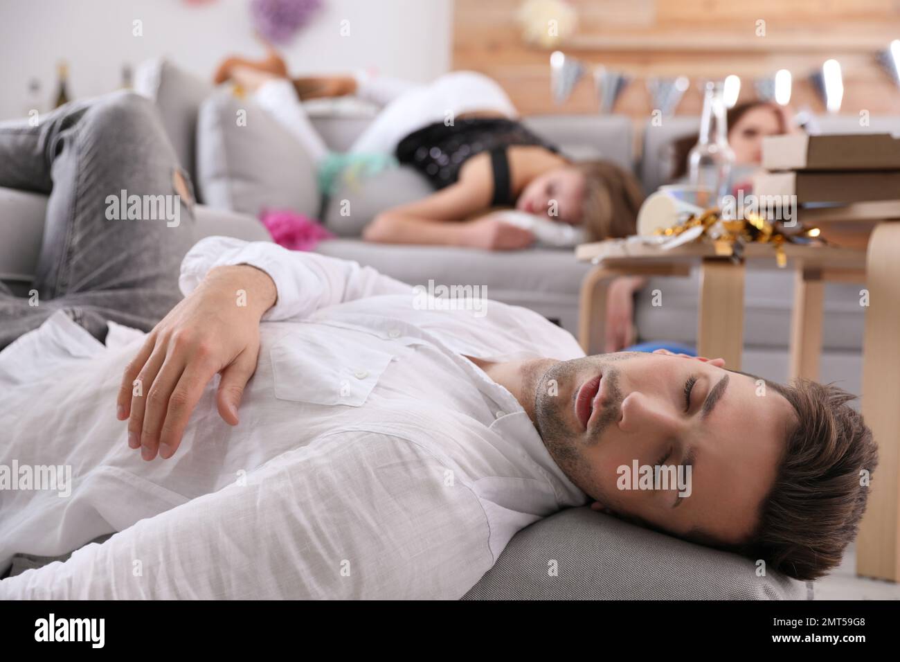 Junger Mann, der nach der Party in einem chaotischen Zimmer schläft Stockfoto