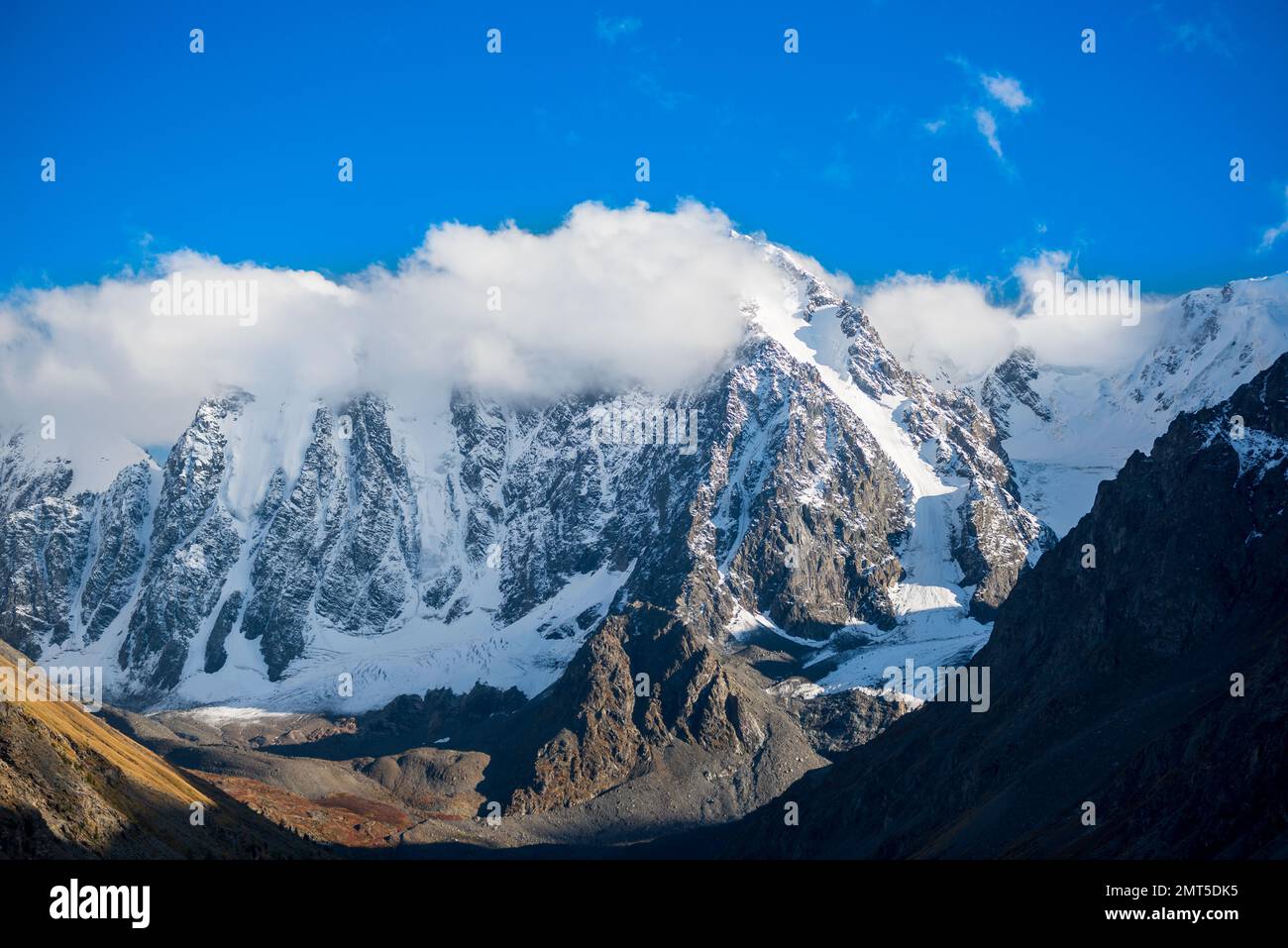 Weiße Wolken bedecken die Gipfel der hohen felsigen Berge mit Schnee und Gletschern in Altai an einem hellen Tag. Peaks Dream, Märchen, Schönheit. Stockfoto