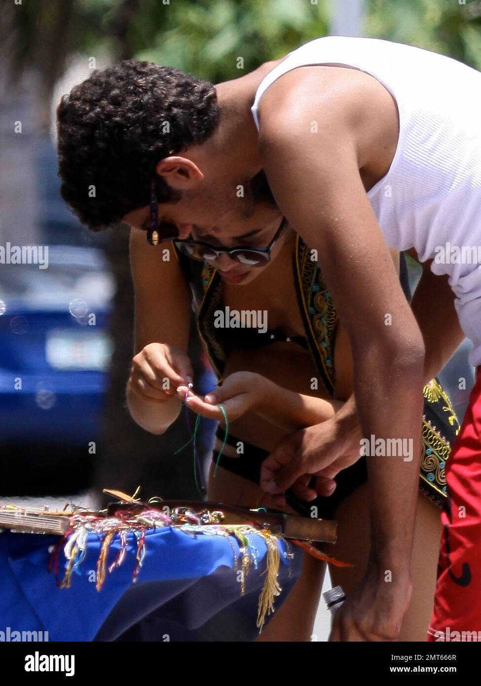 Noah Becker und die Bikinizone Rafaela Remy Sanchez halten an einem Straßenstand, um an einem gemeinsamen Tag am Strand Schnurarmbänder zu kaufen. Rafaela nimmt sich die Zeit, das gewählte Armband um Noahs Handgelenk zu binden, bevor sie abhauen. Miami Beach, Florida 6/7/11. Stockfoto