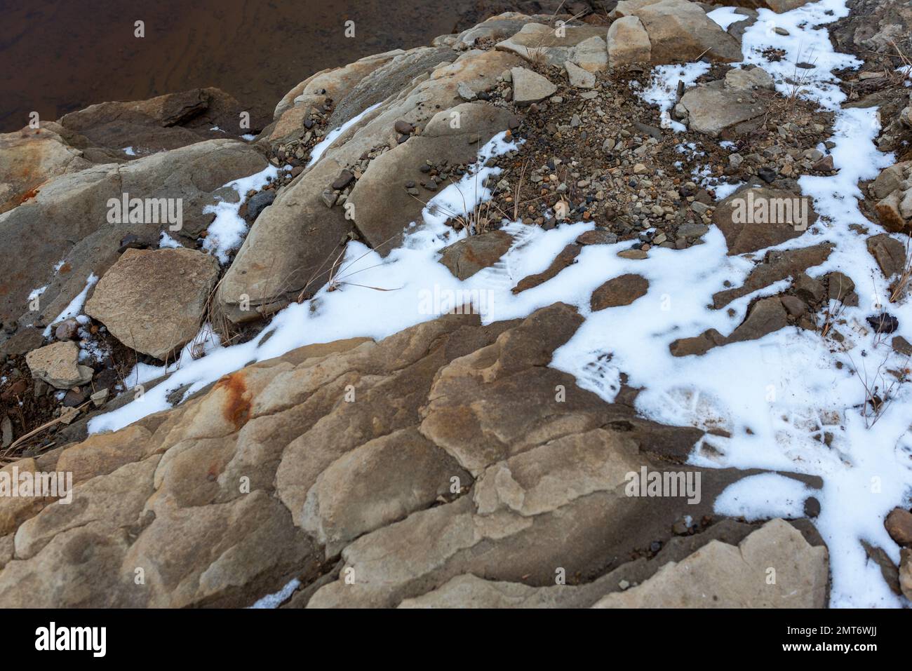 Felsgestein am Ufer mit klarem, schneebedeckten Wasser. Stockfoto