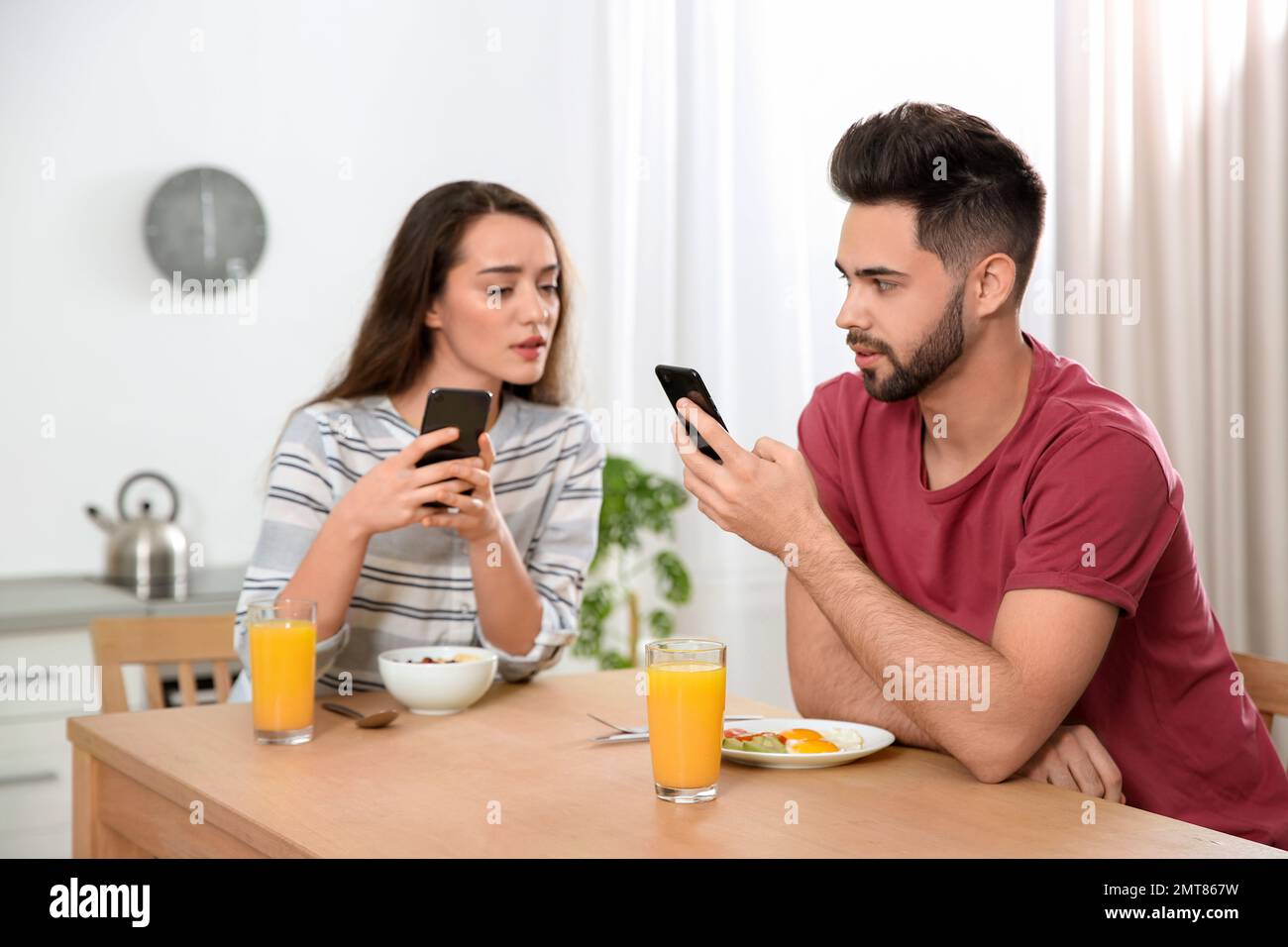 Misstrauische junge Frau, die zu Hause in das Smartphone ihres Freundes schaut Stockfoto