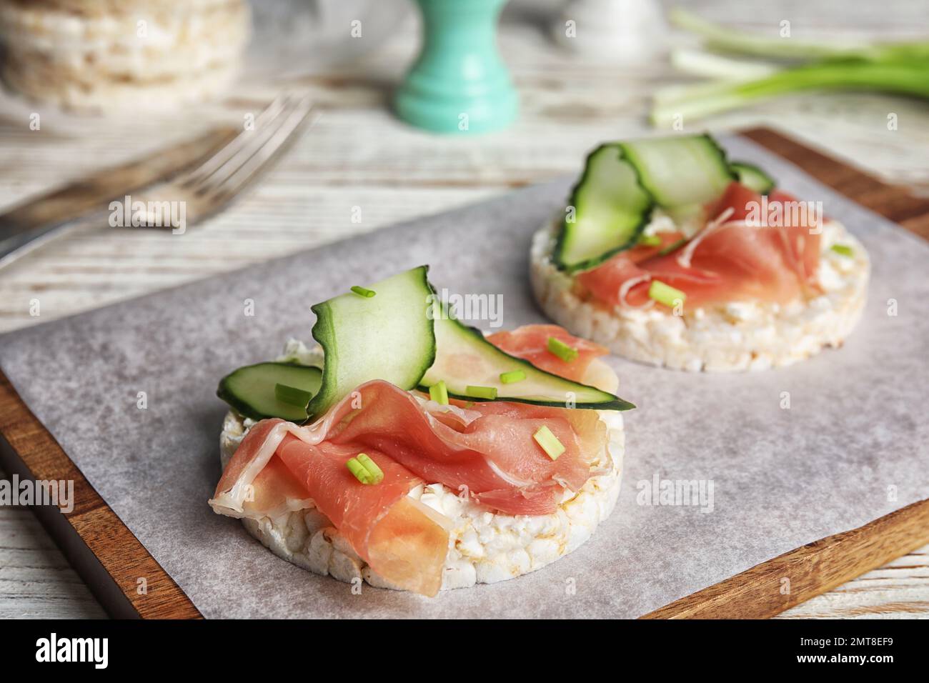 Gepuppte Reiskuchen mit Prosciutto und Gurke auf Holzbrett, Nahaufnahme Stockfoto