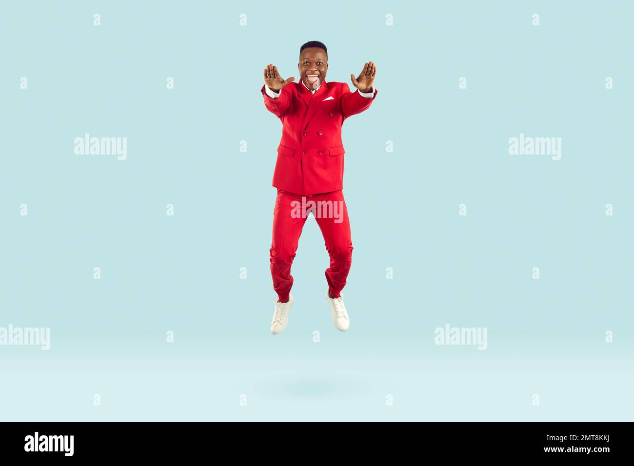 Lustiger, eleganter afroamerikanischer Mann, der Spaß hat, auf pastellblauem Hintergrund zu hüpfen. Stockfoto