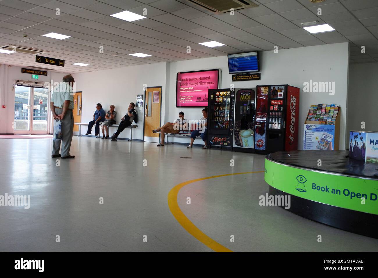 Leute warten in der Ankunftshalle am Flughafen Exeter - John Gollop Stockfoto