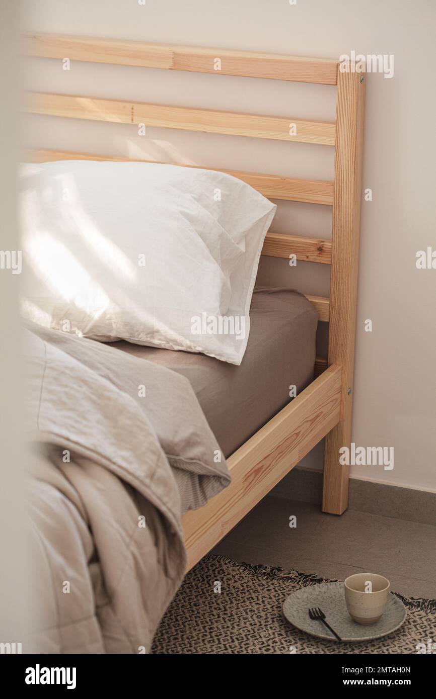 Morgens Holzbett mit beiger Bettwäsche nach dem Frühstück, Nahaufnahme. Echtes Leben, Chaos-Konzept. Stockfoto