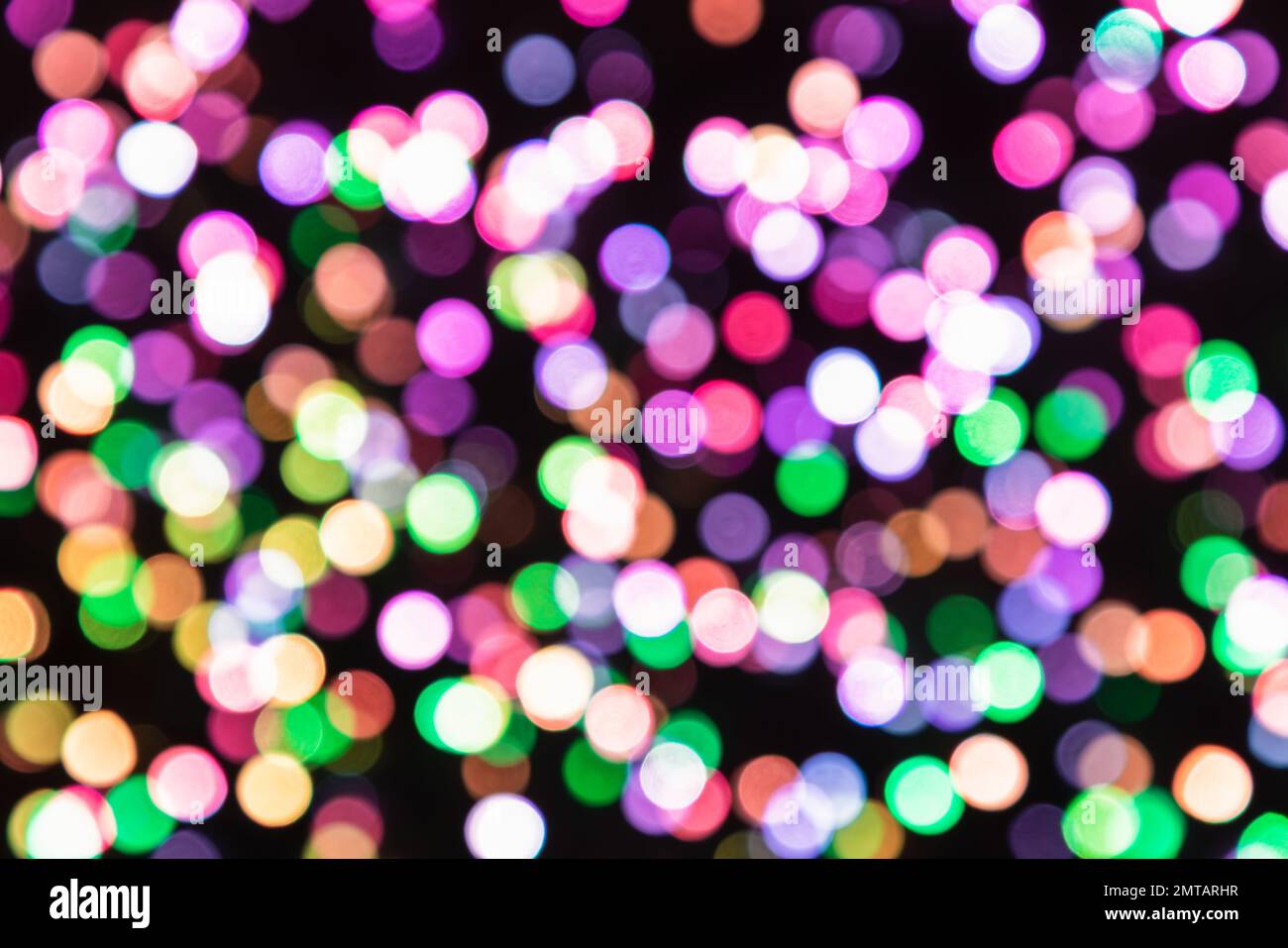 Mehrfarbige Bokeh-Kreise in Rosa, Lila, Grün und Warmweiß überlagern sich auf einem schwarzen Hintergrund und erzeugen eine festliche abstrakte Lichttextur. Stockfoto