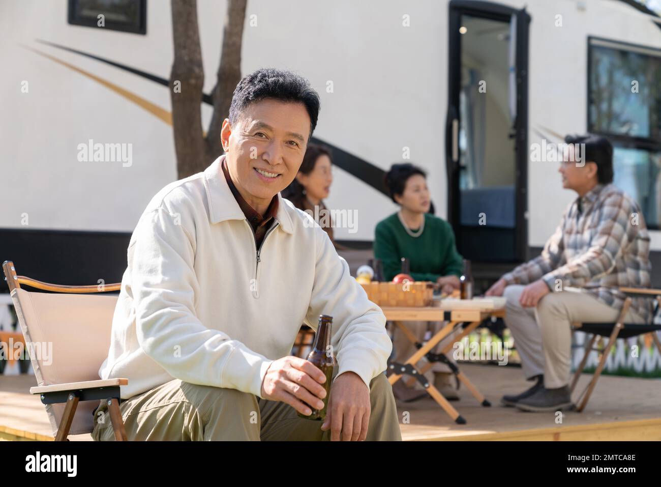 Eine Gruppe alter Leute, die auf einem Campingplatz sitzen und Bier trinken Stockfoto