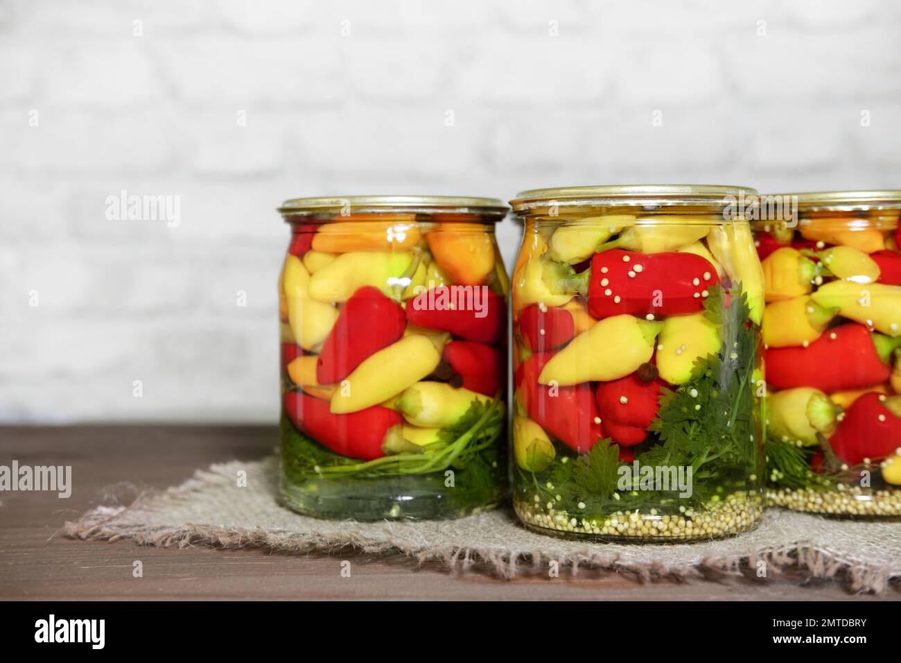Mini-Chili-Paprika in Rot-, Gelb- und Orangenfarben, in Glasdosen mit Kräutern auf einem Holztisch. Hausgemachte eingelegte Paprika im asiatischen Stil. Vorb Stockfoto