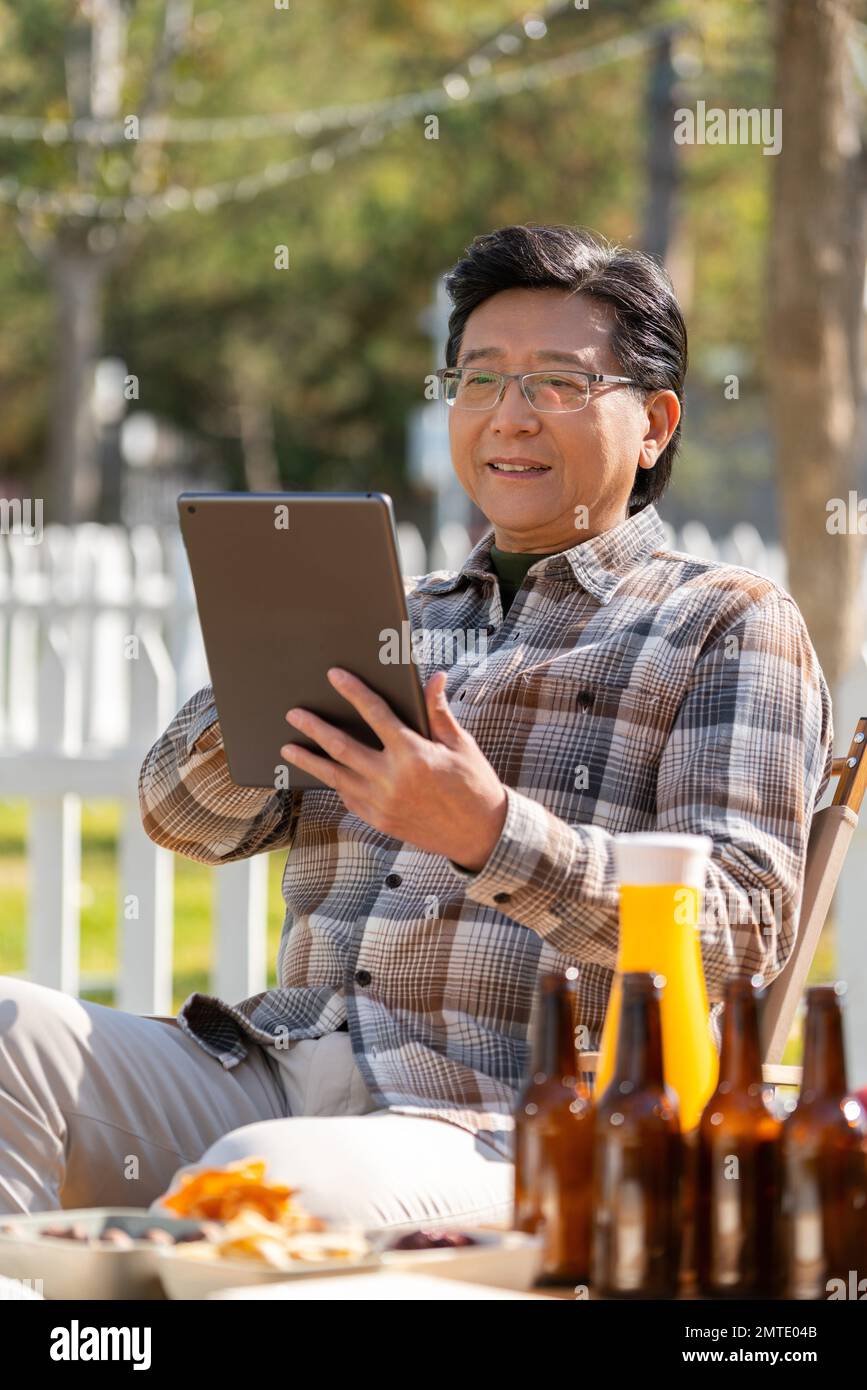 Ein älterer Mann saß in einem Camping draußen im Hof, um Tablets zu sehen Stockfoto