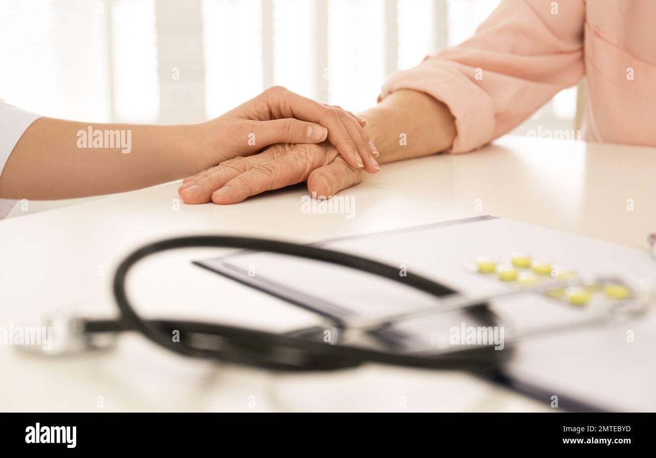 Doktor hält die Hand eines älteren Patienten in der Praxis, Nahaufnahme Stockfoto