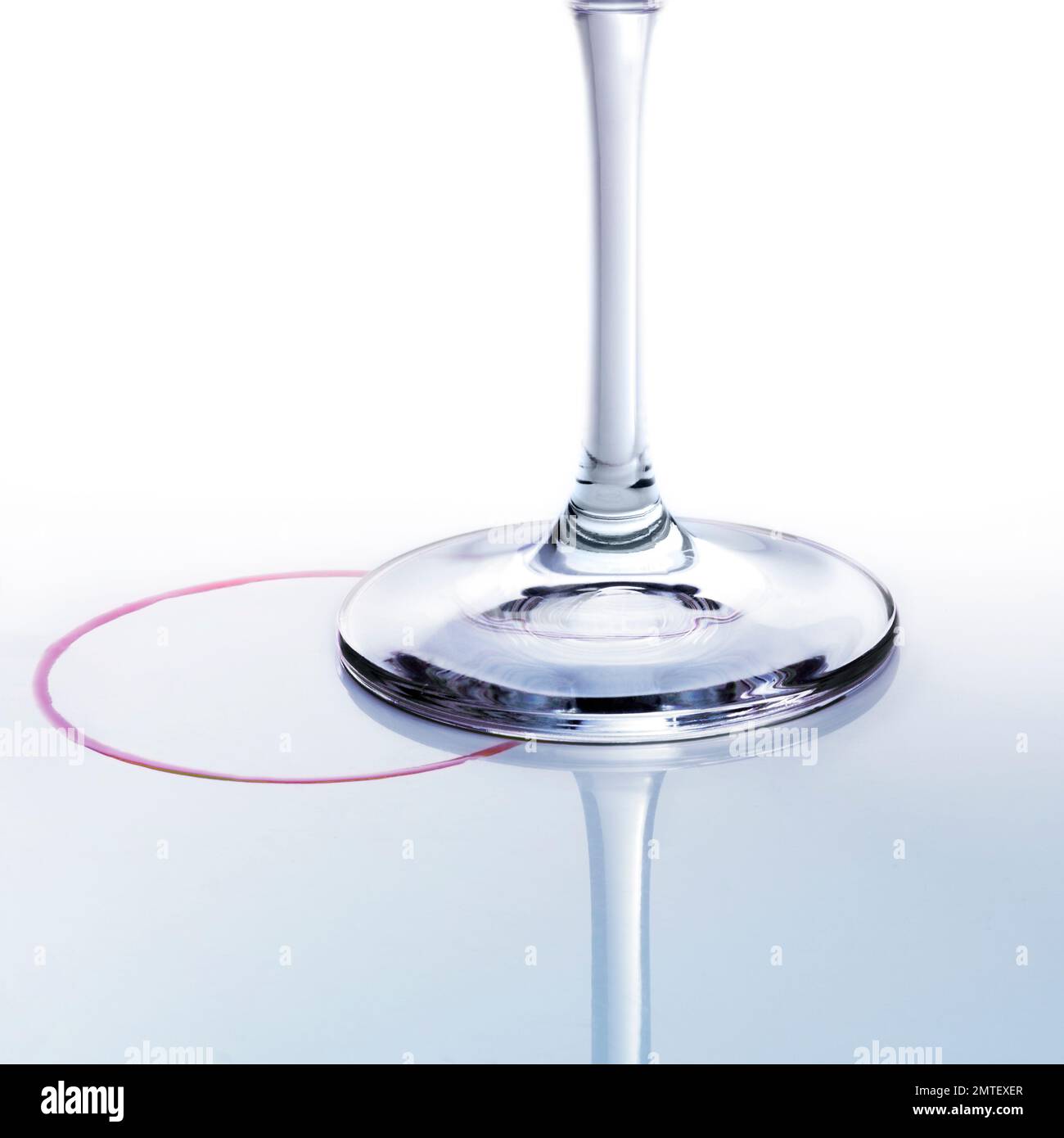 Kreative Nahaufnahme von Weinglas Basis, runde Fleck von Rotwein über reflektierende blaue Farbe Oberfläche. Stockfoto